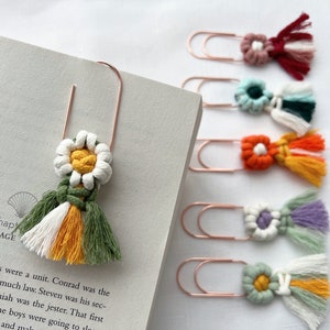 May include: Six colorful crocheted flower bookmarks with tassels attached to gold metal paper clips. The bookmarks are in shades of red, green, blue, orange, purple, and yellow.