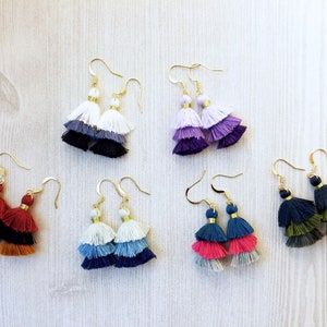 Puede incluir: Conjunto de seis pares de pendientes de borla en capas en varios colores, incluyendo blanco, negro, morado, rojo, azul y verde. Cada pendiente tiene tres capas de borlas.