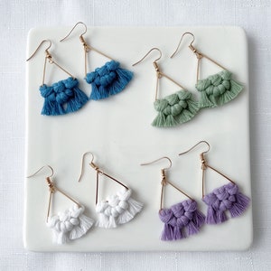 May include: Six pairs of triangle-shaped earrings with fringe. The earrings are made of gold-colored metal and have a variety of colors, including blue, green, white, and purple.