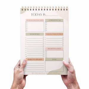 May include: A spiral-bound notepad with a gold coil, featuring sections for daily planning. The notepad includes areas for students, guardians, tasks, meetings, projects, and notes. The text "TODAY IS" is at the top, with the Blooming Mindsets logo at the bottom.
