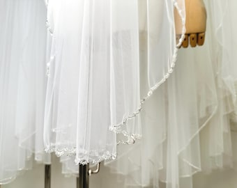 May include: A white bridal veil with a beaded edge. The veil is layered and has a delicate, flowing design.