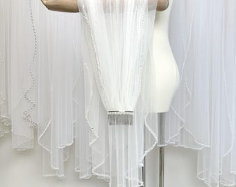 May include: A white bridal veil with a comb, displayed on a mannequin. The veil is made of sheer fabric and is embellished with small, sparkling accents along the edges. The comb is silver-toned.