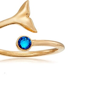 Op de afbeelding: Een gouden ring met een blauwe edelsteen en een walvisstaartontwerp.