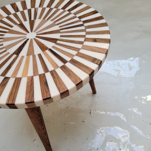 May include: A round wooden side table with a white and brown geometric pattern on the top. The table has three legs.