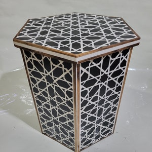 Könnte beinhalten: Ein sechseckiger Beistelltisch mit einem geometrischen Muster in Schwarz und Weiß. Der Tisch ist aus Holz und hat eine braune Oberfläche.