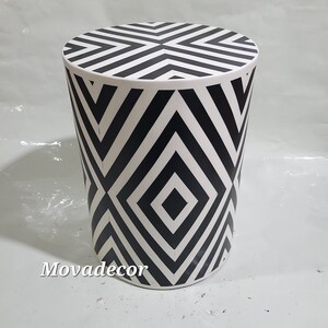 Puede incluir: Taburete cilíndrico con estampado geométrico en blanco y negro. El patrón está formado por diamantes y rayas repetidos.