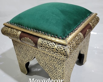 Pode incluir: Um pufe quadrado com uma tampa de veludo verde e uma base de madeira esculpida. A base é decorada com padrões florais intrincados e um acabamento dourado e castanho.