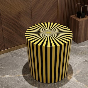 May include: A cylindrical stool with a yellow and black striped pattern. The top of the stool features a sunburst design. The stool is a decorative furniture piece, suitable for various interior settings.