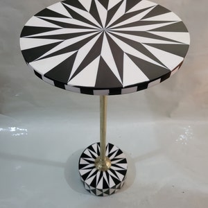 Puede incluir: Una mesa auxiliar con un diseño geométrico en blanco y negro y una base de metal dorado. La mesa tiene un diseño de estrella.