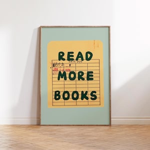 May include: A framed poster with the words "READ MORE BOOKS" in dark green letters. The text is on a yellow library card design, set against a light green background. The frame is a light brown color.