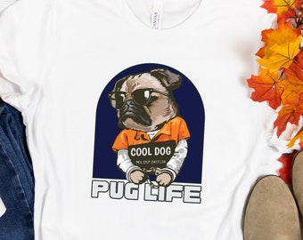 Puede incluir: Camiseta blanca con un gráfico de un pug con un mono naranja y un retrato que dice "Cool Dog". El texto "Pug Life" está impreso debajo del gráfico.
