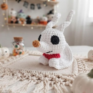 May include: A white crocheted ghost dog figurine with long ears, a round tan nose, black circular eyes, and a red collar. The ghost dog is crafted with visible yarn stitches and has a smooth, rounded head and body shape, presented in a seated position.