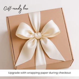 May include: A brown cardboard gift box with a white satin ribbon tied in a bow. The box has the text "Gift-ready box" printed on the top. The text "Upgrade with wrapping paper during checkout" is printed below the box.