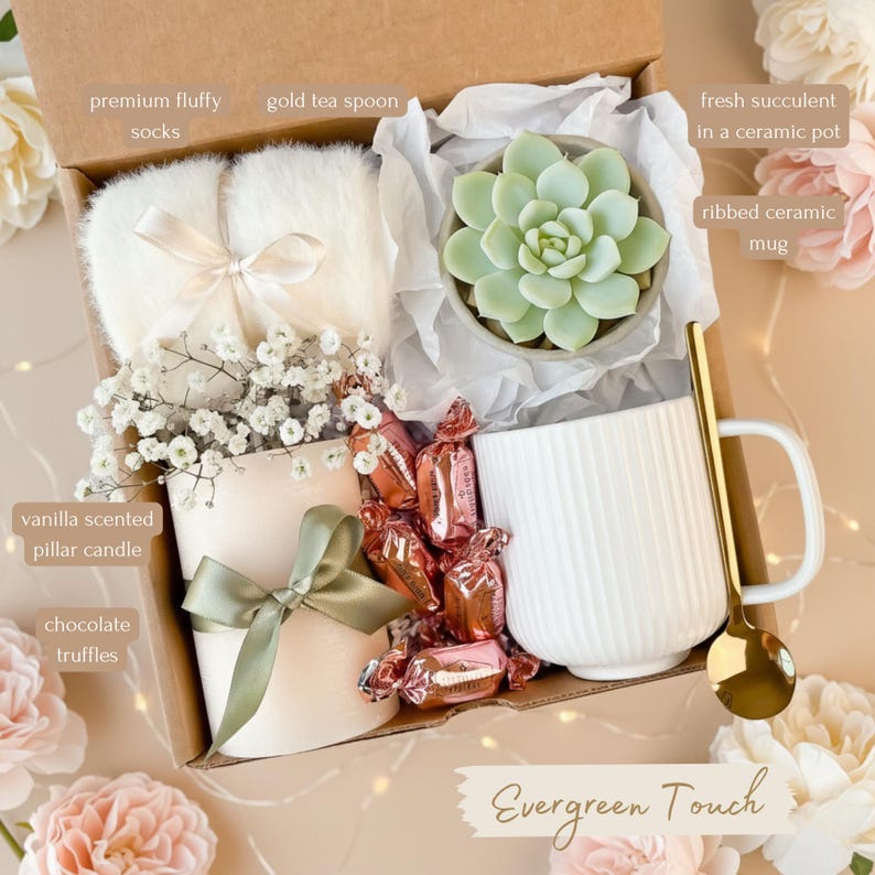 May include: A gift box with a variety of items. Includes fluffy socks, a vanilla-scented pillar candle, chocolate truffles, a gold tea spoon, a succulent in a ceramic pot, and a ribbed ceramic mug. The box is labeled "Evergreen Touch".