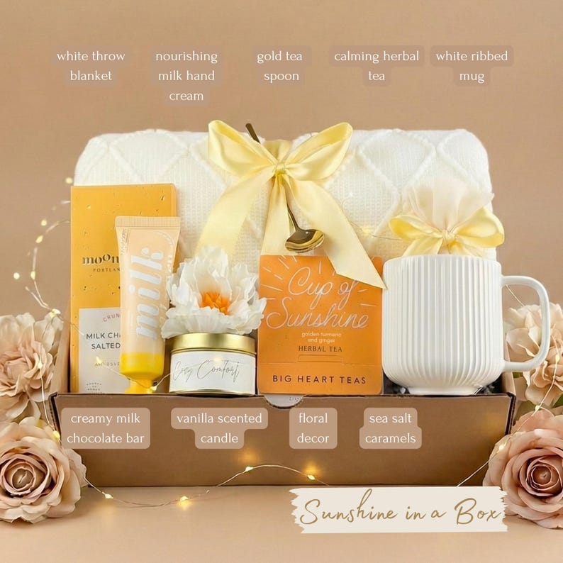 May include: A gift box filled with self-care items. Includes a white throw blanket, mug, tea, hand cream, candle, chocolate bar, and floral decor. The box is tied with a yellow bow and includes the text "Sunshine in a Box".