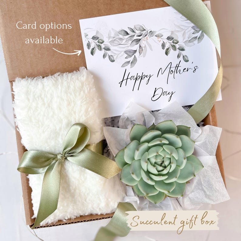 Puede incluir: Una caja de regalo con una suculenta, un art&iacute;culo blanco y esponjoso atado con una cinta verde y una tarjeta que dice "Happy Mother's Day". La caja es marr&oacute;n y la tarjeta tiene un dise&ntilde;o floral. El texto en la caja dice "Card options available."