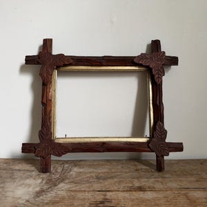 May include: A rectangular picture frame constructed from dark brown wood with a textured, branch-like appearance. The corners feature carved leaf motifs, and the inner edge of the frame is finished with a smooth, metallic gold-colored border.