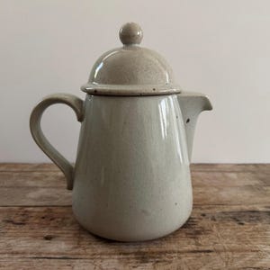 May include: A white ceramic teapot with a lid and a handle. The teapot has a speckled glaze and a rounded shape.