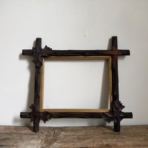 May include: A rectangular picture frame featuring a dark brown, textured outer border that resembles tree branches with carved leaf accents at the corners. The inner border of the frame is finished in a smooth, metallic gold tone.