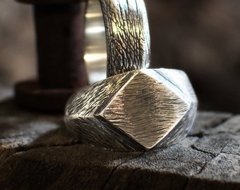 May include: A silver ring with a textured, geometric design. The ring is sitting on a piece of wood.