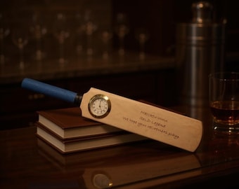 May include: A wooden cricket bat with a blue grip and a clock face embedded in the wood. The bat rests on two brown books. Text on the bat reads "Matthew Innes, SOLD Legend, We hope your retirement stays..."