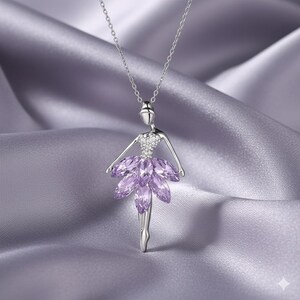 Op de afbeelding: Een zilverkleurige ballerina hangerketting. Het lijfje van de ballerina is bezet met kleine, heldere kristallen en de tutu is gemaakt van paarse marquise-geslepen kristallen. De ketting hangt aan een fijne zilveren ketting, tegen een zijdeachtige, lavendelkleurige achtergrond.