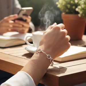 May include: A silver chain bracelet featuring a series of interconnected oval links with a polished metallic finish. The bracelet is worn on a wrist, showcasing the repeating link pattern that forms a continuous loop around the arm.