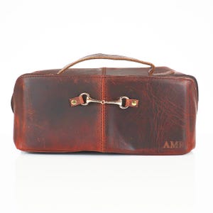 May include: A brown leather travel bag with a gold metal clasp and the initials "AMR" embossed on the front.
