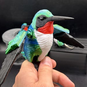 Könnte beinhalten: Eine 3D-gedruckte Kolibri-Figur mit grüner, blauer, weißer, schwarzer und roter Farbe. Der Kolibri ist im Flug mit ausgebreiteten Flügeln dargestellt.
