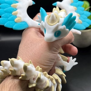 May include: A white and blue articulated dragon toy with wings, a horn, and a halo. The dragon is posed with its wings spread and its head tilted up.