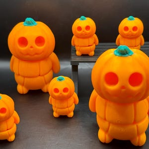 May include: Five orange pumpkin figurines with green stems and black eyes. The pumpkins are stacked on top of each other to form a body. The pumpkins are arranged on a black surface.