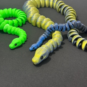 May include: Three 3D printed snake toys. The largest snake is yellow and blue, the middle snake is yellow and black, and the smallest snake is green.