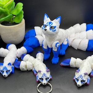 May include: A set of white and blue kitsune figurines with nine tails. The figurines are made of plastic and have a detailed paint job. The tails are segmented and can be posed in different ways.