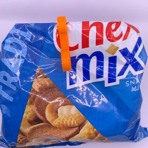 May include: A blue bag of Chex Mix snack mix with an orange plastic bag clip on the top. The bag is crumpled and shows the different types of snacks inside, including pretzels, breadsticks, and peanuts.