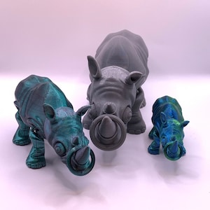 May include: Three 3D printed rhinoceros figurines. The largest is gray, the middle is green and blue, and the smallest is blue and green. All three have rings around their noses.