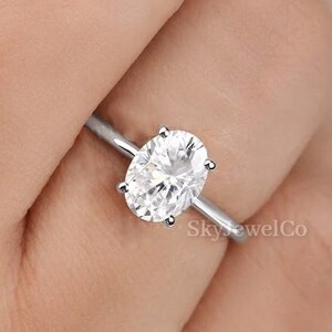 May include: A silver ring with a large oval-shaped clear gemstone. The ring is on a person's finger.