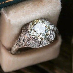 May include: A vintage engagement ring with a large, round, clear diamond center stone surrounded by smaller diamonds. The ring is set in platinum and has a delicate, intricate design.