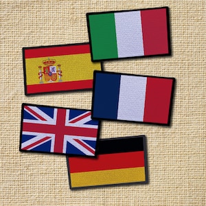 Può includere: Cinque toppe di tessuto con le bandiere di Italia, Spagna, Francia, Regno Unito e Germania. Le toppe sono disposte a scalare su uno sfondo di tessuto beige.
