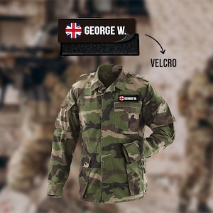 Może przedstawiać: Kamuflażowa kurtka wojskowa z naszywką na rzep z napisem "GEORGE W." i małą flagą Unii.