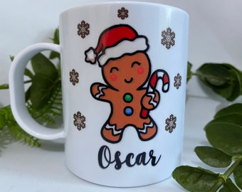 May include: White ceramic mug with a gingerbread man design. The gingerbread man is wearing a red Santa hat and holding a candy cane. The mug has a brown snowflake pattern and the name "Oscar" is written on the bottom.