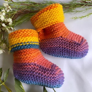 May include: A pair of knitted baby booties with a rainbow colour pattern. The booties are made with a soft yarn and have a fold-over cuff.