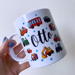 May include: White ceramic mug with a blue handle. The mug features a design of various vehicles, including a bus, lorry, car, tractor, and digger. The name "Otto" is written in black cursive on the mug.