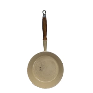 May include: A white enamelled cast iron frying pan with a wooden handle. The pan has a slightly speckled finish.