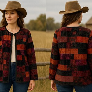 May include: A patchwork jacket in shades of red, black, and orange. The jacket has a round neckline and long sleeves. The model is wearing a brown hat and blue jeans. The background is a field with a wooden fence and a small building.