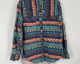 May include: A long-sleeved button-down shirt with a colorful geometric pattern. The shirt features a mandarin collar and a curved hem. The pattern includes teal, burgundy, gold, and navy blue zigzags and other shapes.