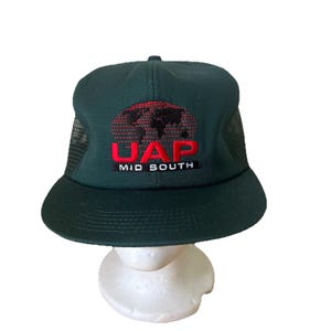 Könnte beinhalten: Dunkelgrüne Trucker-Mütze mit schwarzem Mesh-Rücken und gebogenem Schirm. Auf der Vorderseite der Mütze befindet sich der rote Text "UAP" über "MID SOUTH" und ein Weltkarten-Design.