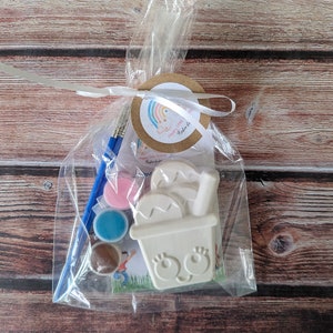 May include: A white ceramic paint-your-own flower pot with a happy face and a small paintbrush, three small paint pots, and a tag that says "Happy Little Painter Kit".