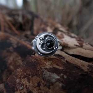 May include: A silver ring with a crescent moon design and a black gemstone in the center.