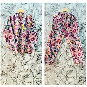 Puede incluir: Un conjunto de pijama rosa con estampado floral. La parte superior tiene un frente abotonado y mangas largas. Los pantalones tienen una cintura elástica.