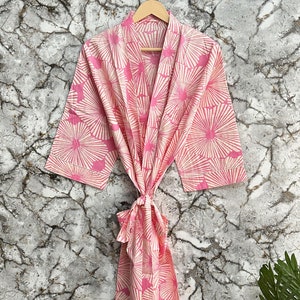May include: A pink and white floral print robe with a tie belt. The robe is made of cotton and has a relaxed fit.